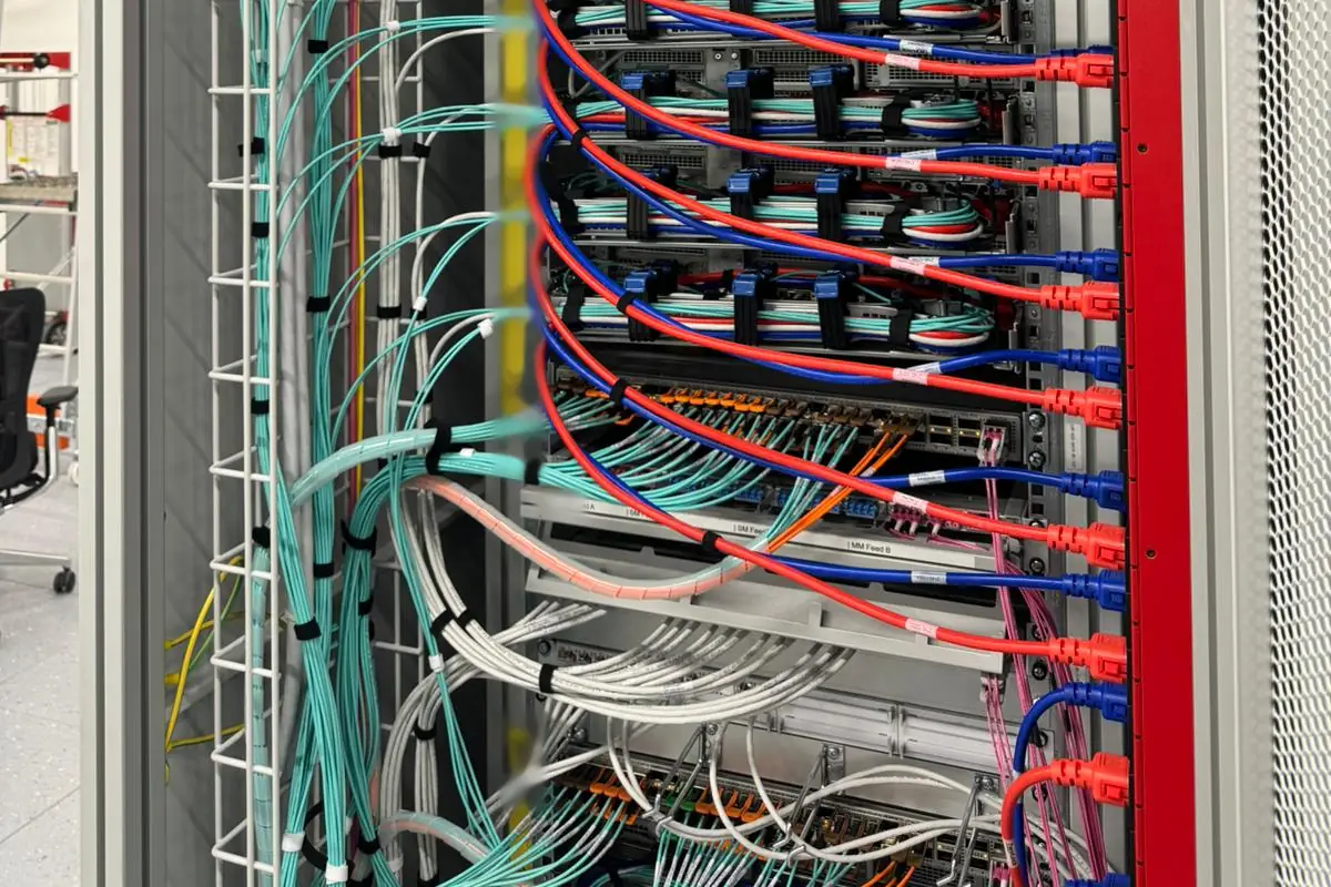 Rear of a rack at a customer site: aqua fibre patch cables fan out of the vertical cable tray to the servers, above a switch and the labelled patch panels for the multimode and singlemode feeds